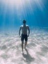 Sporty freediver stay on sandy bottom underwater in ocean with sun rays Royalty Free Stock Photo