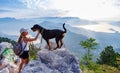 A sporty girl with a backpack stands on the edge of a mountain with a Rottweiler dog Royalty Free Stock Photo