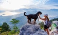 A sporty girl with a backpack stands on the edge of a mountain with a Rottweiler dog Royalty Free Stock Photo