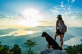 A sporty girl with a backpack stands on the edge of a mountain with a Rottweiler dog Royalty Free Stock Photo