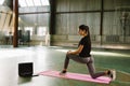 Sporty girl doing online yoga exercises on the mat in empty training gym during the quarantine period of coronavirus Royalty Free Stock Photo