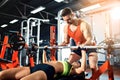 Sporty girl doing weight exercises with assistance of her personal trainer at gym.