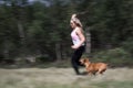 Sporty girl and her dog/pet are running and playing with a stick outdoors in the forest. Royalty Free Stock Photo