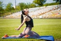 Sporty girl stratching muscles on yoga mat on stadium green lawn. Sport, physical training, healthy way of life, fitness concept. Royalty Free Stock Photo