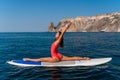 Sporty girl on a surfboard in the sea on a sunny summer day. In a red swimsuit, she sits in the splits on the sap