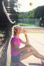 Sporty girl in the tennis uniform throwing up tennis ball while relaxing on the court near net. Relaxing break after Royalty Free Stock Photo