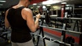 Sporty guy doing lift-ups with curl bar near stand in gym, pumping arm muscles