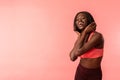 Sporty happy african girl in sportswear holds her hands near her head and looking at the camera isolated over pink Royalty Free Stock Photo