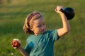 Sporty kid with apple and kettlebell outdoor in summer park. Sport activities at leisure with children. Blonde boy