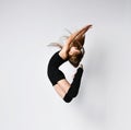Young girl gymnast in black sport body and uppers jumping and making dymnastic pose in air over white background