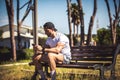 Sporty man personal trainer sitting looking at his phone on a bench in an outdoor park. Muscle body and well defined. Sporty