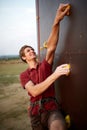 Sporty man practicing rock climbing in gym on artificial rock training wall outdoors. Young talanted smiling climber guy Royalty Free Stock Photo