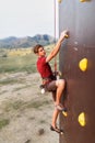 Sporty man practicing rock climbing in gym on artificial rock training wall outdoors. Young talanted climber guy on Royalty Free Stock Photo