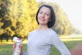 Sporty mature woman hold bottle with water outdoor on sunny day in the park Royalty Free Stock Photo
