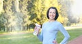 Sporty mature woman hold bottle with water outdoor on sunny day in the park