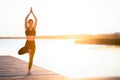 Sporty middle aged female practicing yoga on a wooden pier on sunset Royalty Free Stock Photo