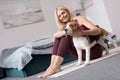 sporty middle aged woman stroking dog while sitting on yoga mat Royalty Free Stock Photo