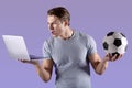 Sporty millennial man disappointed at his football team defeat, watching soccer game on laptop, violet studio background Royalty Free Stock Photo