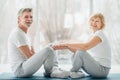 Sporty senior couple sitting on the mat in the white fitness gym and doing stretching while and looking at camera and smiling. Royalty Free Stock Photo