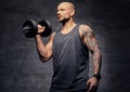 Sporty shaved head tattooed male doing biceps workout with dumbbell.