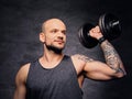 Sporty shaved head tattooed male doing biceps workout with dumbbell.