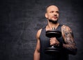 Sporty shaved head tattooed male doing biceps workout with dumbbell.