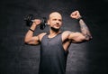 Sporty shaved head tattooed male doing shoulder workout with dumbbell.