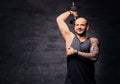 Sporty shaved head tattooed male doing triceps workout with dumbbell.