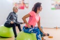 Sporty slim women taking part in gym fitness class exercising sitting on physioballs doing alternated biceps curl with