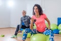 Sporty slim women taking part in gym fitness class exercising sitting on physioballs doing alternated biceps curl with