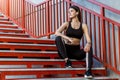 Sporty slim young beautiful woman in black fashionable sportwear sitting on the red stairs and relaxing during outdoor exercises