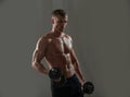 Sporty torso, man with dumbbells. Portrait of young athlete doing exercise with dumbbell at dark studio