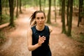 Sporty woman ages 20-30 with long hair runs in forest among trees and looking into camera