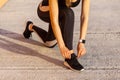 Sporty woman in black sporwear at morning on street standing on knee and preparing for training, tying shoelaces on sneakers Royalty Free Stock Photo