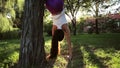 Sporty woman doing yoga exercises with handstand headfirst near the tree.