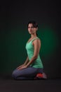 Sporty woman, fitness woman sitting on a dark background with green backlight