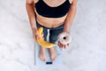 Sporty woman with a perfect body measuring body weight on electronic scales and holding a donut and a yellow banana