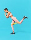 Sporty woman with resistance band loop workouts on blue background