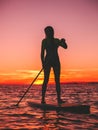 Sporty woman stand up paddle boarding at dusk on a flat warm quiet sea with beautiful sunset Royalty Free Stock Photo