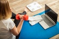 Sporty woman using dumbbells making fitness at home via laptop by remote video call online. Young woman losing weight by online