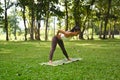 Sporty yogini woman practices yoga, standing Diver Yoga pose with green foliage trees landscape in background