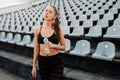 Sporty young attractive girl in sportswear relaxing after hard workout sit and drink water from bottle after running on a stadium Royalty Free Stock Photo