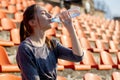 Sporty young attractive girl in sportswear relaxing after hard workout sit and drink water from special sport bottle after running Royalty Free Stock Photo