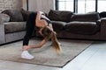 Sporty young female doing stretching exercise bending forward during home workout