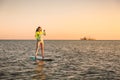 Sporty young girl stand up paddle surfing with beautiful sunset colors Royalty Free Stock Photo