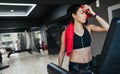 Sporty young woman athlete running on treadmill in the gym, wiped off with a red towel and listening the music by her earphones. Royalty Free Stock Photo