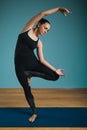 Sporty young woman doing stretching standing. Slim girl practicing yoga indoors on blue background. Calm, relax, healthy Royalty Free Stock Photo