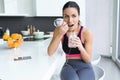 Sporty young woman eating strawberry smoothie while listening to music in the kitchen at home Royalty Free Stock Photo