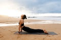 Sporty young woman practicing yoga outdoors, making upward facing dog pose while meditating on beach by seaside Royalty Free Stock Photo