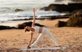 Sporty young woman practicing yoga outdoors, standing in triangle pose, exercising on sea beach on mat, full length Royalty Free Stock Photo